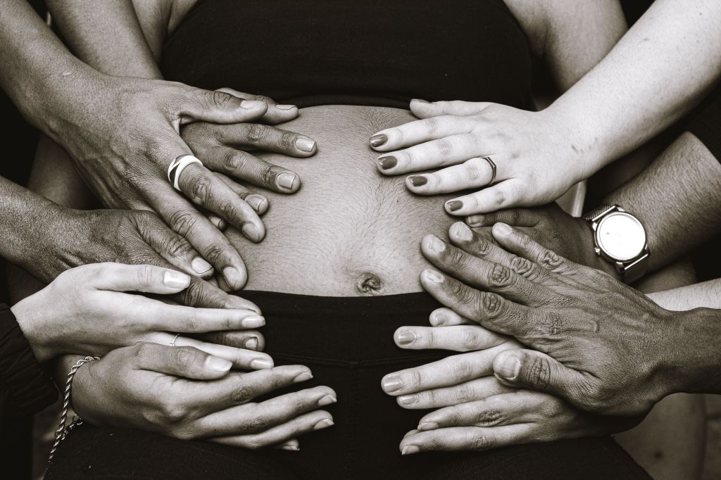Photo of several hands framing a pregnant person's stomach